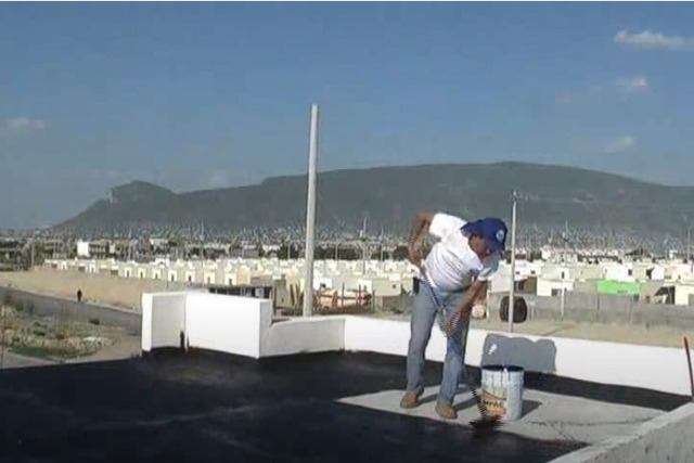 Roofing worker adding asphalt on commercial flat roof